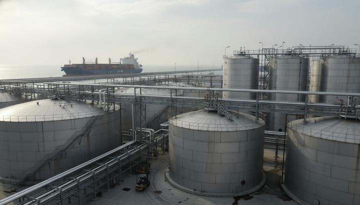 Промышленные резервуары для хранения биодизеля в порту на фоне грузового судна, символизирующие международную торговлю биотопливом.
